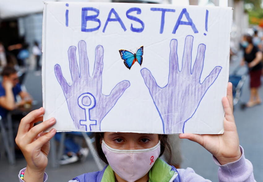 Una niña sostiene un cartel en el que se lee "Basta" mientras la gente se manifiesta contra la violencia machista