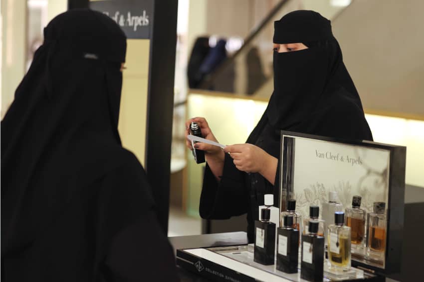 Una dependiente le vende un perfume a una mujer en Arabia Saudí. Ambas van vestidas con niqab