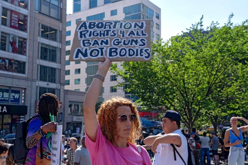 Una mujer sostiene un cartel que dice "derecho al aborto para todxs, prohíban las armas, no los cuerpos"