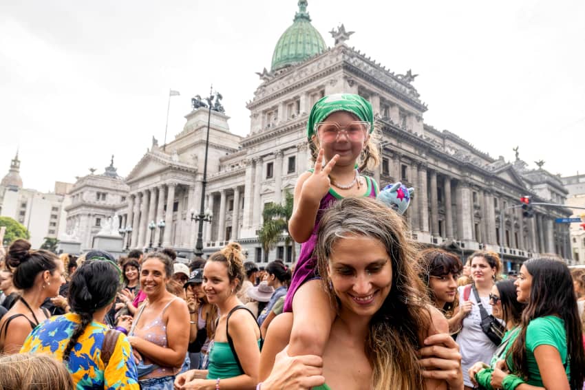 Una niña hace el signo de la victoria mientras es cargado sobre los hombros de una madre durante el Día Internacional de la Mujer.