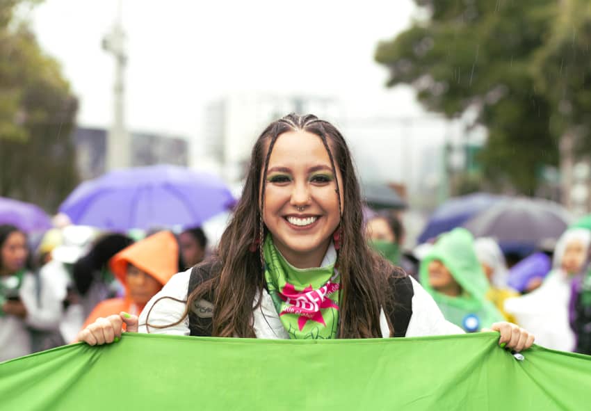 Mujer manifestante sonríe mientras sostiene una pancarta en una marcha feminista en Quito contra la discriminación del aborto