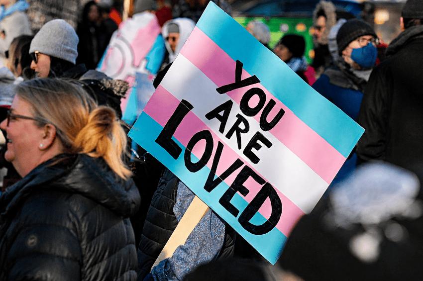 Persona sostiene cartel con bandera trans en protesta contra la homofobia y la violencia LGBTIQ+