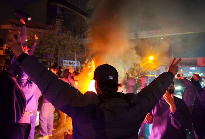 Personas se concentran de noche en una calle de Teherán alrededor de una hoguera durante una protesta.