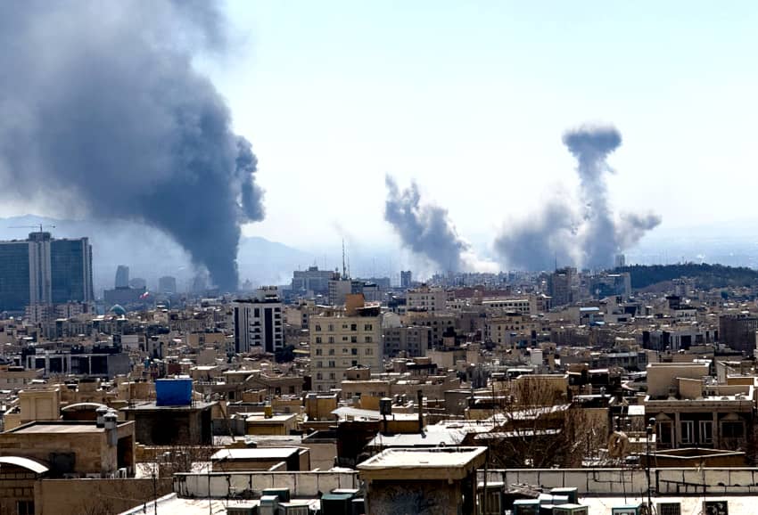 Vista general de Teherán a plena luz del día con varias columnas de humo negro y gris elevándose sobre la ciudad después de explosiones.