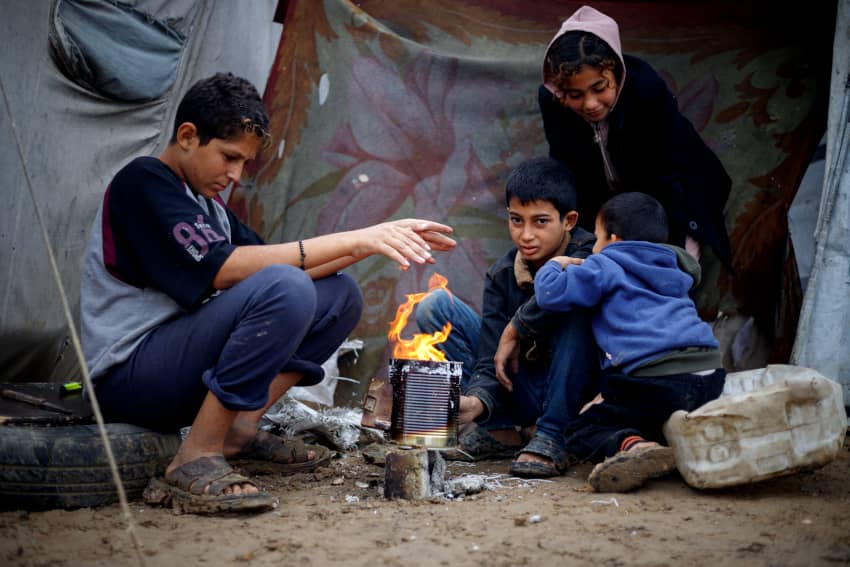 Niños desplazados se calientan alrededor de un fuego en un campamento en Gaza