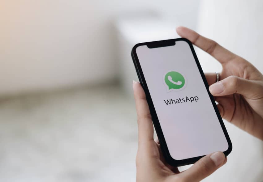 Una persona sostiene un teléfono móvil con el logotipo y el nombre de WhatsApp en pantalla.