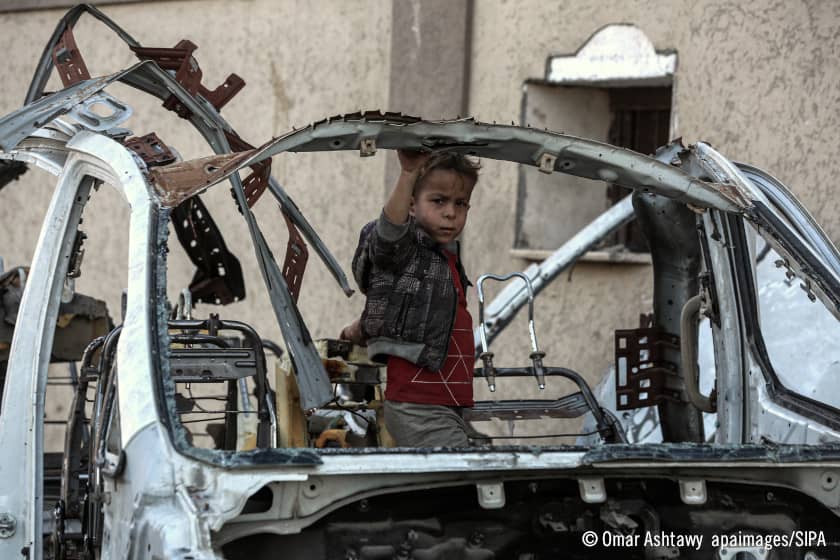 Niño detrás de un coche destruido