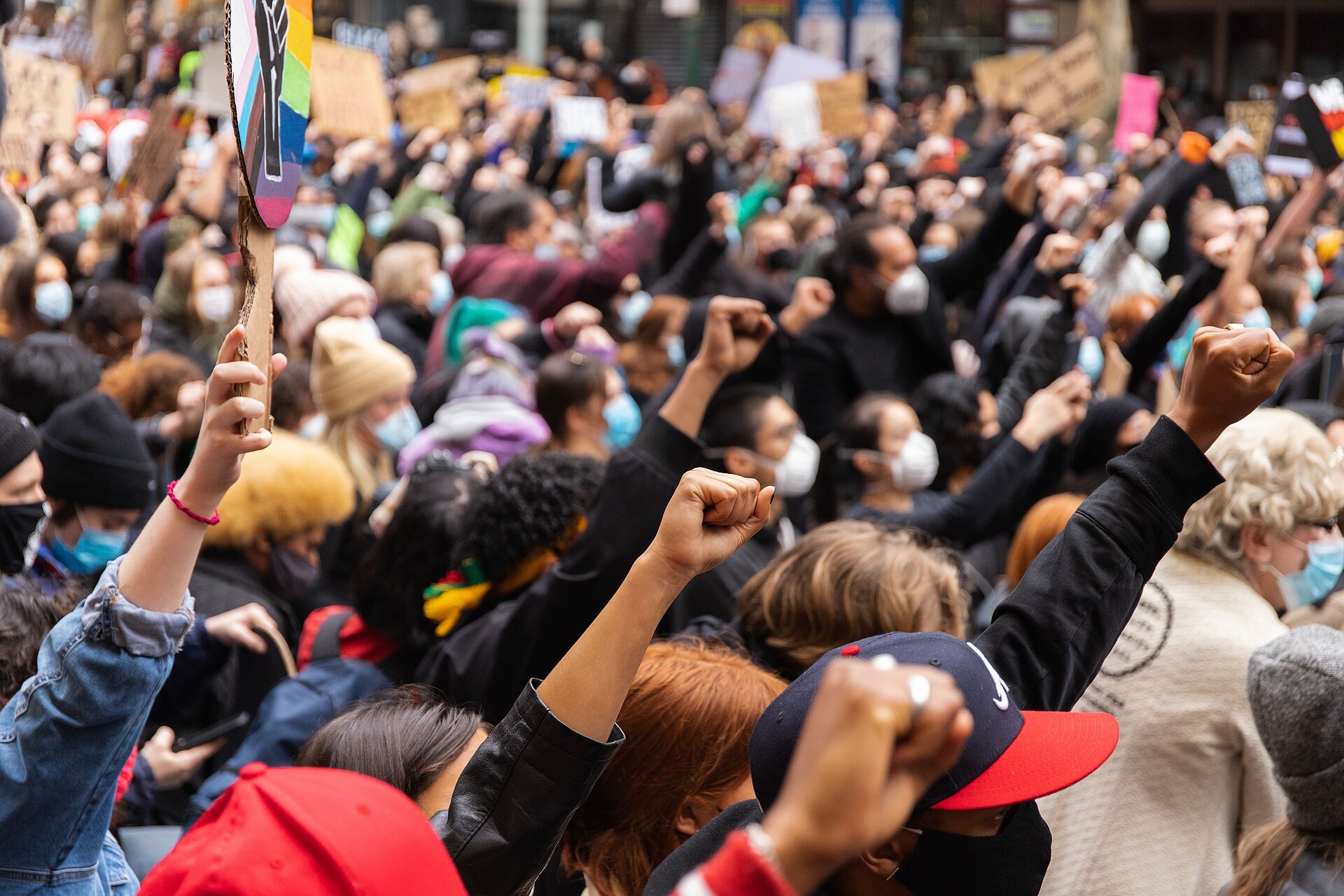 multitud recorre una avenida durante una manifestación, con pancartas, carteles y banderas en alto.